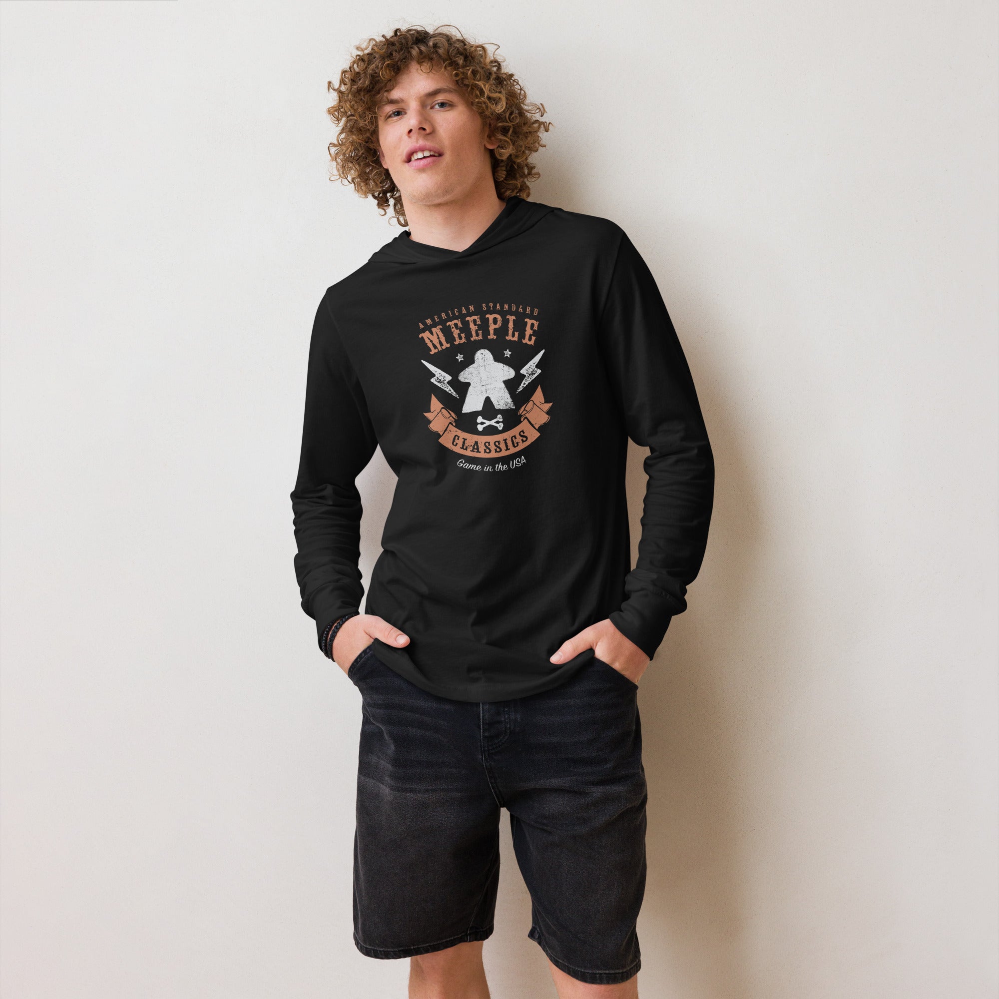 Model leaning against wall and wearing long sleeve American Meeple Classics t-shirt